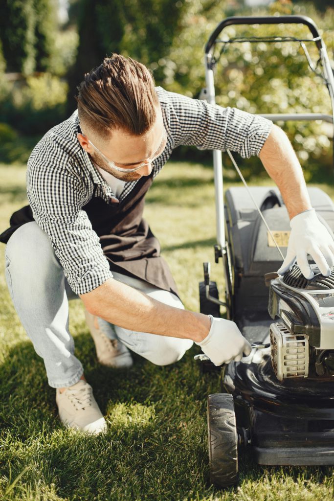 pexels-photo-5163431-5163431 Man in a garden repairing lawn mower on sunny day, ideal for gardening and maintenance themes.